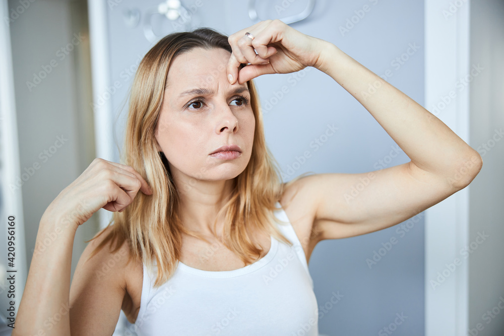 Blonde woman checking wrinkles on her forehead Blonde woman checking wrinkles on her forehead