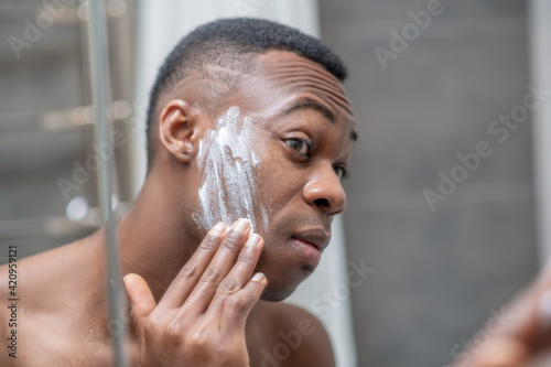 African american young handsome man shaving in the bathroom