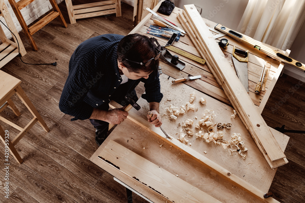 Middle-aged man carpenter working in a workshop with chisel and hammer Middle-aged man carpenter working in a workshop with chisel and hammer