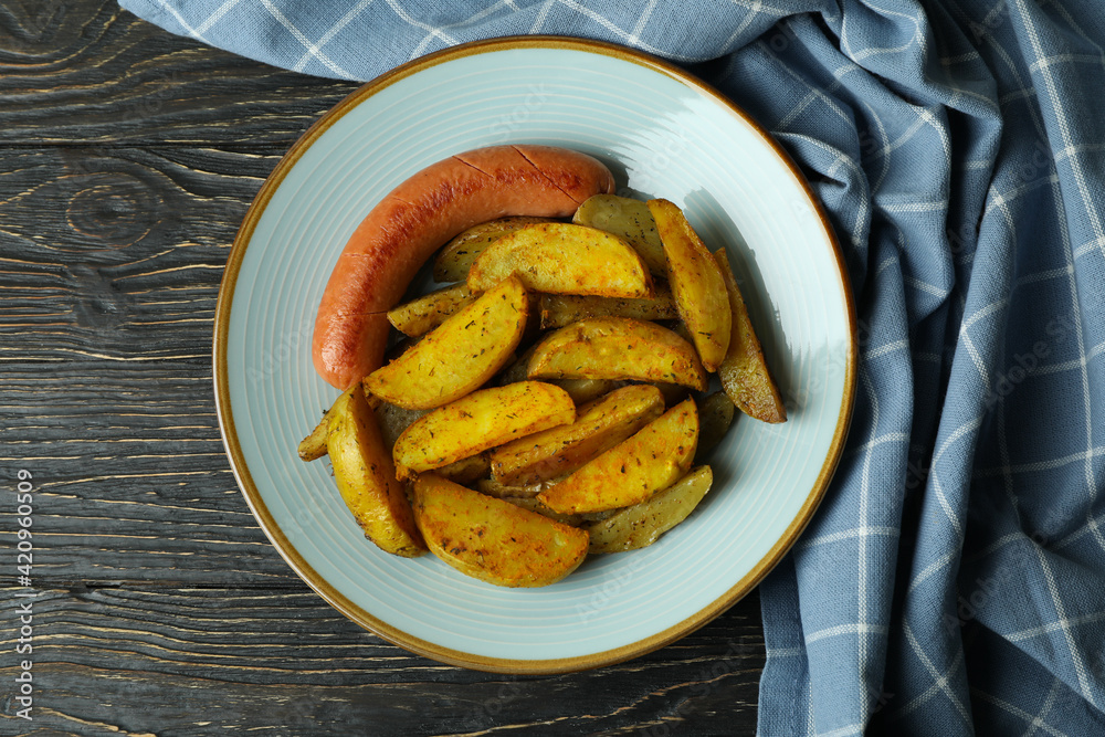 Plate with fried potato and sausage, and kitchen towel on wooden background Plate with fried potato and sausage, and kitchen towel on wooden background