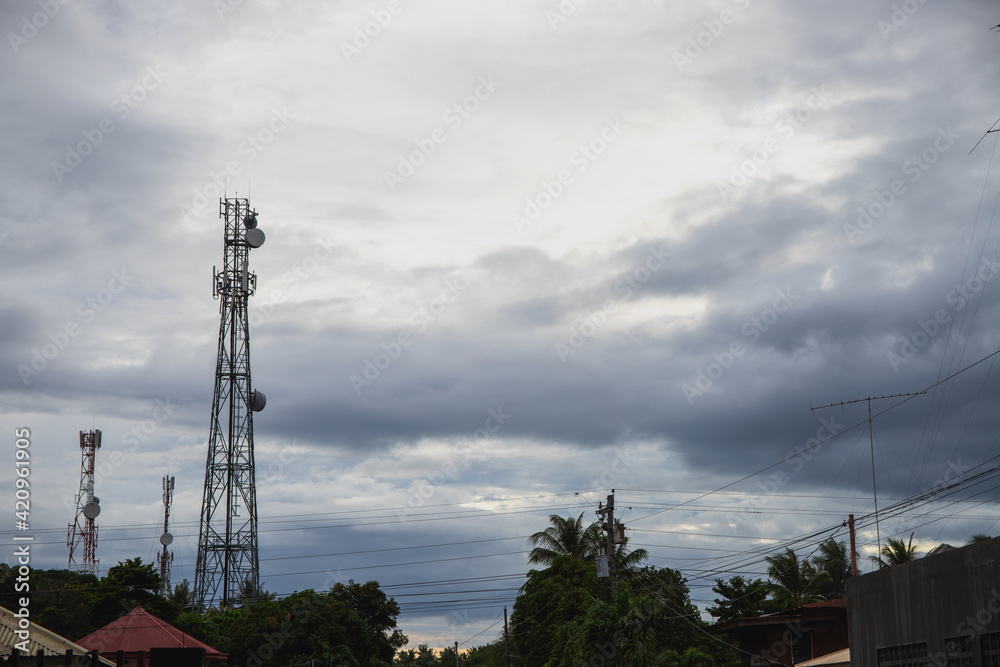 Electric pillar over trees and house roofs, grey cloudy sky panorama. Skyline with communication towers. Internet and radio broadcasting towers on rainy sky. Bad weather influence on internet speed