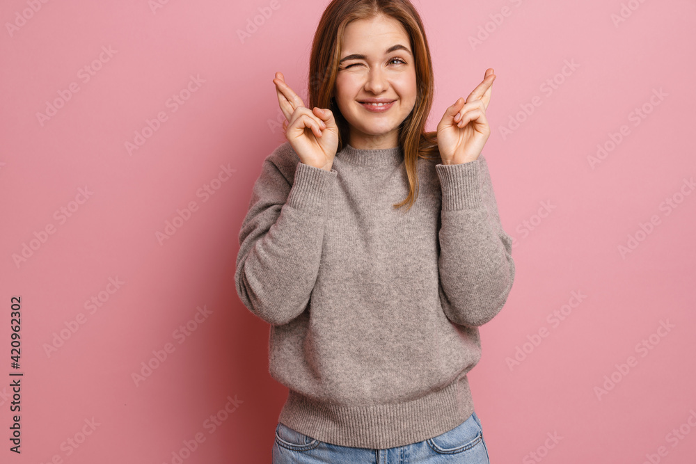 Ginger happy woman winking and holding fingers crossed for good luck