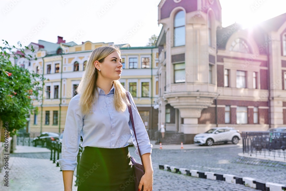 Outdoor young business woman with laptop bag walking along street