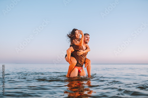 Happy young fit couple embrace each other with love in the sea or ocean at summer sunset. Romantic mood, tenderness, relationship, vacation concept. photo