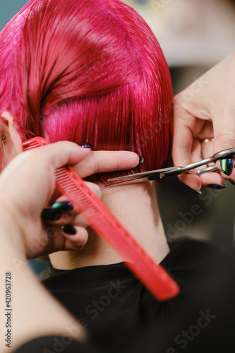 The female hairdresser cuts the bob haircut on bright red painted hair.
