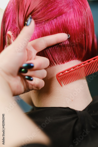 The female hairdresser cuts the bob haircut on bright red painted hair.