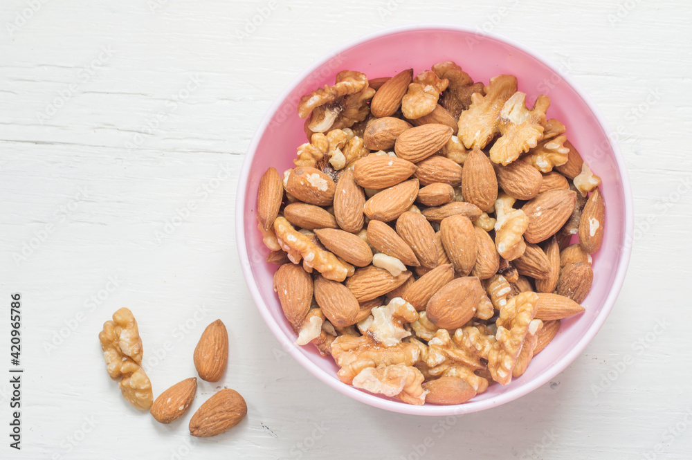 Walnuts and almonds in a pink bowl on a white wooden background. Vegetarian food.