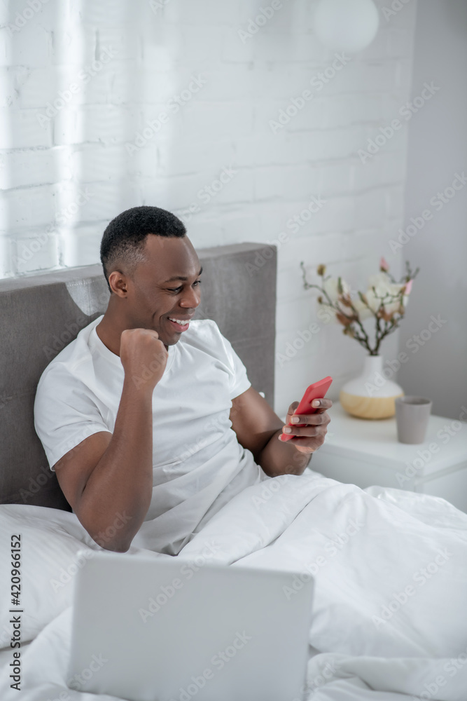 A young man in white tshirt lying in bed and working remotely A young man in white tshirt lying in bed and working remotely
