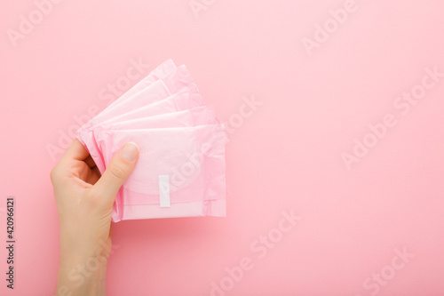 Young adult woman hand holding packs of sanitary towel on light pink table background. Pastel color. Closeup. Empty place for text. Top down view. photo