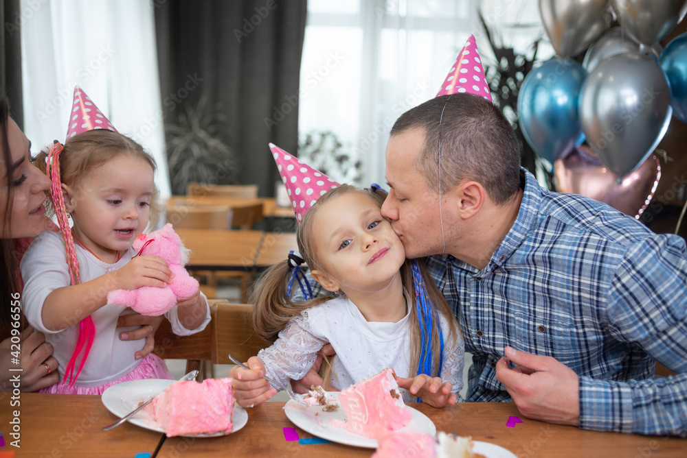 Obraz premium A Caucasian family is sitting at home at the table, party hats are worn on their heads. Family birthday concept.