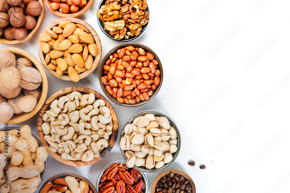 Assortment of nuts in bowls. Cashews, hazelnuts, walnuts, pistachios, pecans, pine nuts, peanuts, macadamia, almonds, brazil nuts. Food mix on white background, top view, copy space Assortment of nuts in bowls. Cashews, hazelnuts, walnuts, pistachios, pecans, pine nuts, peanuts, macadamia, almonds, brazil nuts. Food mix on white background, top view, copy space
