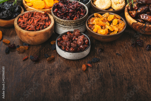 Healthy food snack: dried fruits, natural sun dried organic mix of dried apricots, figs, raisins, dates, cranberries, cherries, goji berries, prunes in bowls on wooden background, top view