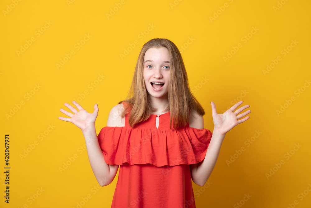 Cute girl raises palms from joy, happy to receive awesome present from someone, shouts loudly, dressed in summer dress, isolated on yellow background. Excited teen girl yells. Cute girl raises palms from joy, happy to receive awesome present from someone, shouts loudly, dressed in summer dress, isolated on yellow background. Excited teen girl yells.