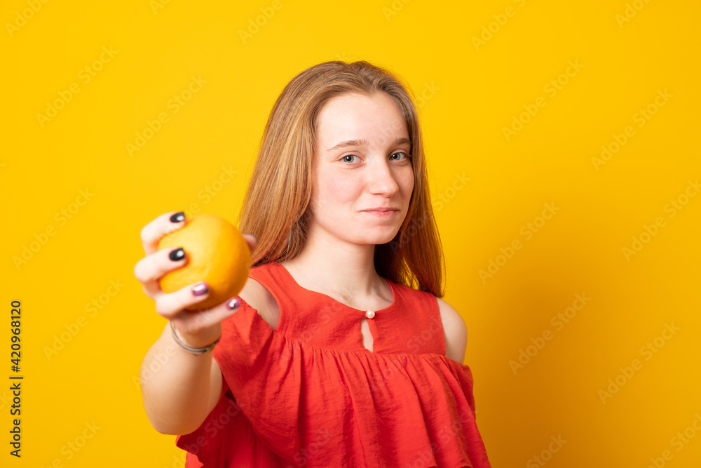 Cute girl teenager holds out an orange fruit on a yellow background. Cute girl teenager holds out an orange fruit on a yellow background.