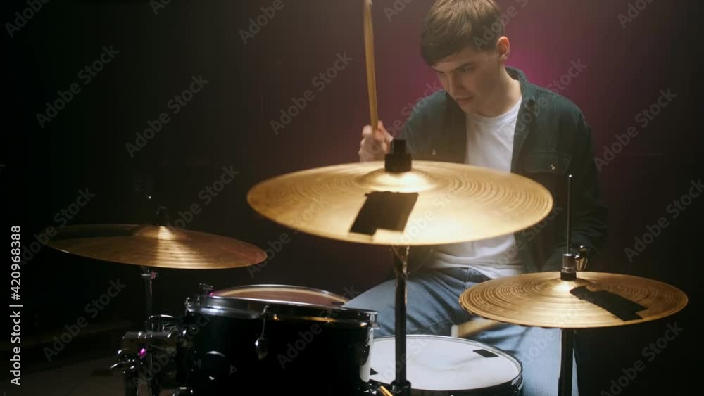 Drummer playing the drum set in a dark room on a black background.