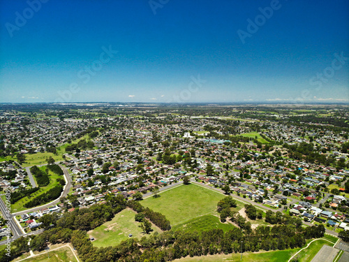 Angled aerial photograph of green grassed area amongst suburban houses on sunny summer day with blue sky