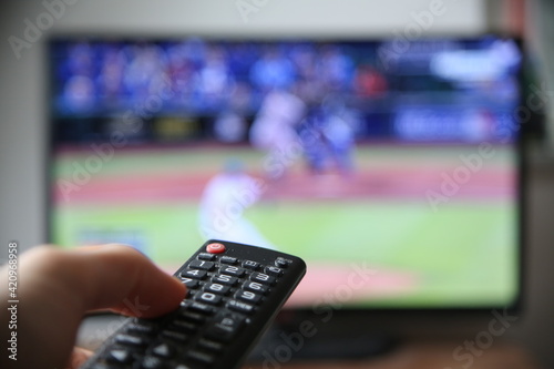Baseball im Fernsehen schauen. Finger auf die Lauter-Taste auf der Fernbedienung. (Fokus auf der Fernbedienung)