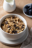 Muesli with chocolate in white bowl served with blueberry and milk on the table . Healthy breakfast concept.