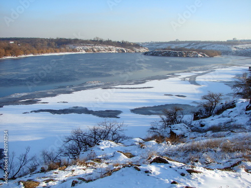Fototapeta Naklejka Na Ścianę i Meble -  Panorama from the top of the hill of the frozen Dnieper covered with strong ice and dressed in a snow blanket on a frosty sunny day at sunset.