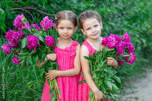 Girls in pink dresses with bouquets of peonies in the countryside
