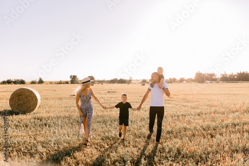 happy family walks in the field near the haystack at sunset, mom dad and two sons, the family is happy with smiles on their faces, hug the children