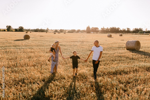 happy family walks in the field near the haystack at sunset, mom dad and two sons, the family is happy with smiles on their faces, hug the children