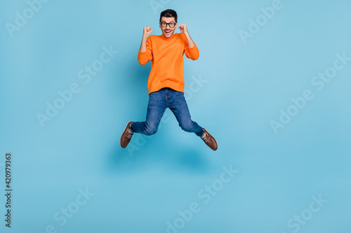 Full body portrait of impressed handsome guy jump high fists up celebrate isolated on blue color background © deagreez