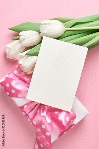 Blank invitation card with copy space and white tulip flowers with gift box on pink paper background © nikavera