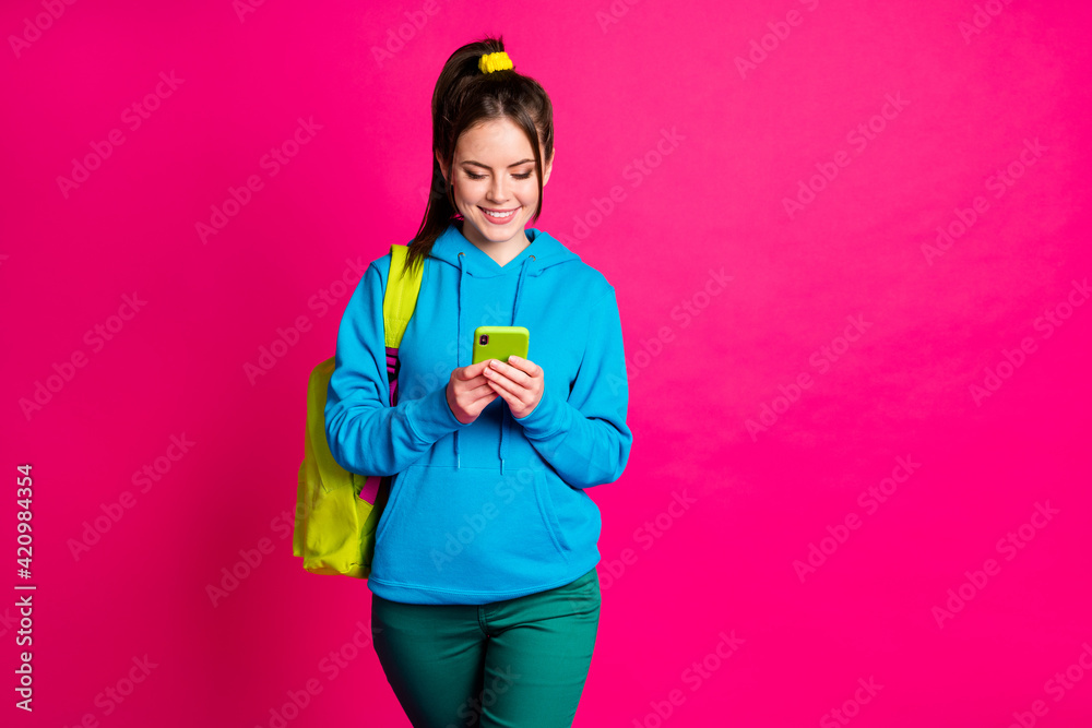 Photo of shiny pretty young woman dressed blue hoodie backpack typing modern gadget isolated vibrant pink color background Photo of shiny pretty young woman dressed blue hoodie backpack typing modern gadget isolated vibrant pink color background