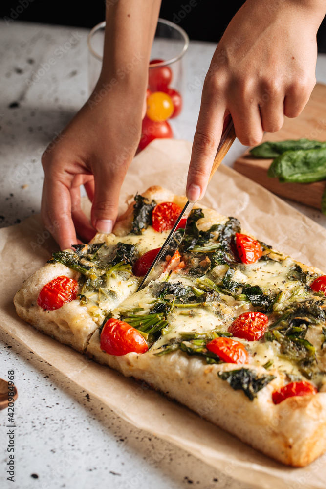 Slicing italian topping bread focaccia with spinach and tomatoes