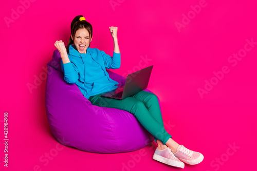 Full length photo of lucky lady wear blue sweater relaxing violet beanbag modern device rising fists isolated pink color background