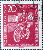 GERMANY, DDR - CIRCA 1959 : a postage stamp from Germany, GDR showing a mail delivery woman with a moped with houses. Postage Stamp Day 1959