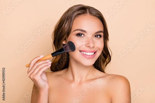 Photo of young happy smiling beautiful woman doing contouring apply blush on cheeks isolated on beige color background photo