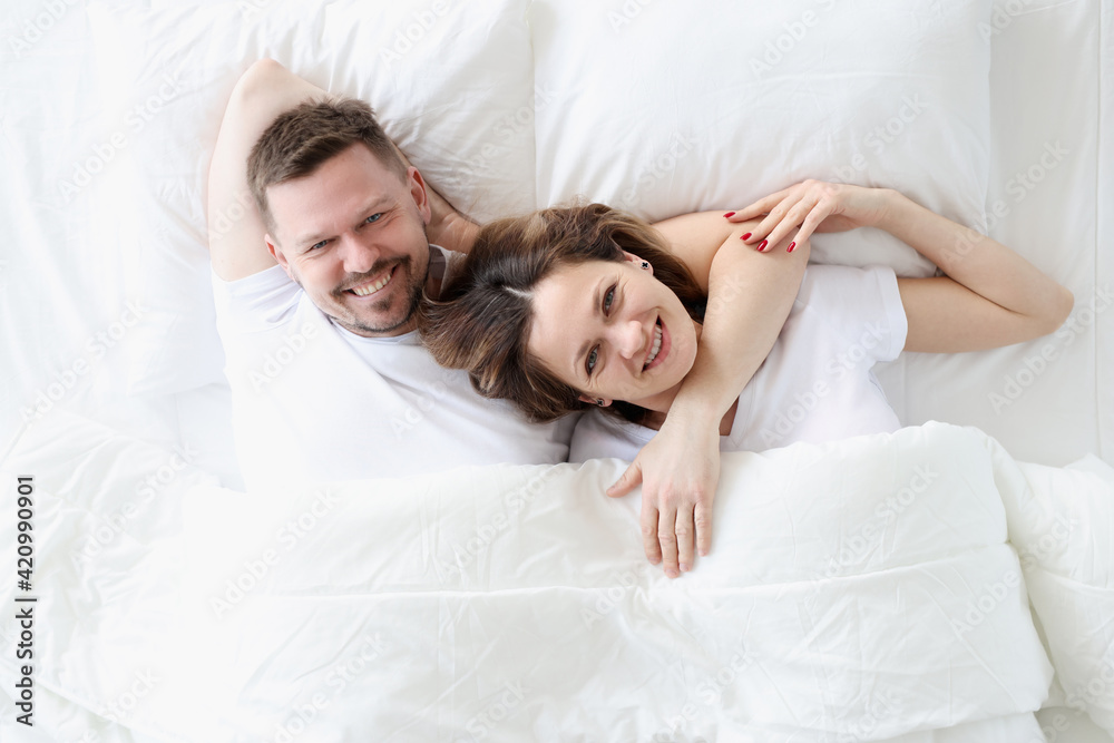 Smiling happy man and woman lie on large white bed Smiling happy man and woman lie on large white bed