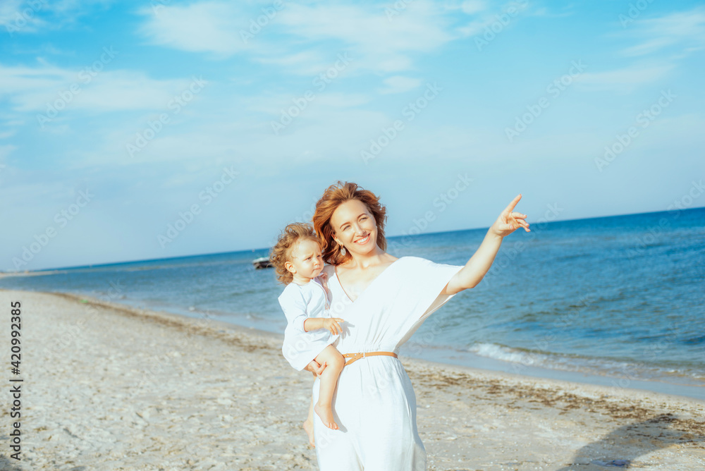 Mom is holding and smiling a little daughter 1 year old with red curly hair in light clothes in the summer on the beach. Happy childhood. Travel and family vacations
Mom is holding and smiling a little daughter 1 year old with red curly hair in light clothes in the summer on the beach. Happy childhood. Travel and family vacations