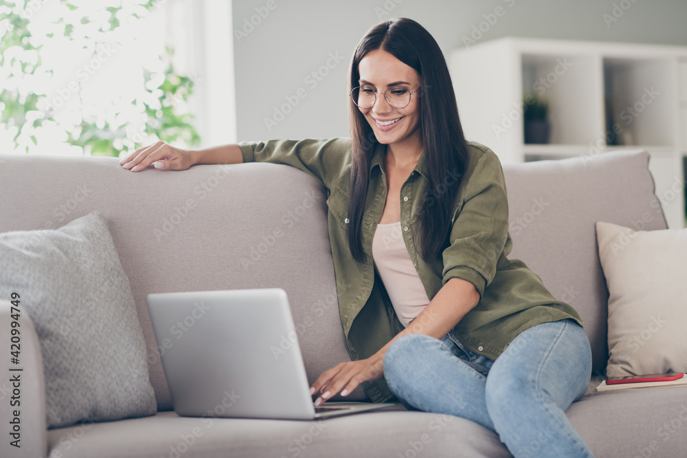 Full body profile side photo of young woman happy positive smile sit couch look browse laptop work project indoors Full body profile side photo of young woman happy positive smile sit couch look browse laptop work project indoors