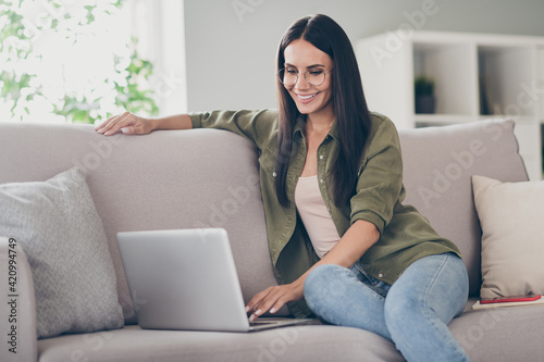 Full body profile side photo of young woman happy positive smile sit couch look browse laptop work project indoors © deagreez