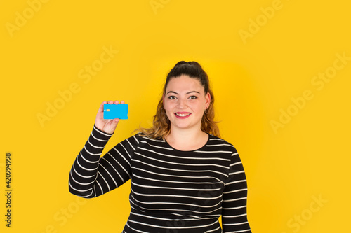 Mujer joven y sonriente sosteniendo una tarjeta de crédito sobre un fondo amarillo liso y aislado. Vista de frente y de cerca. Copy space