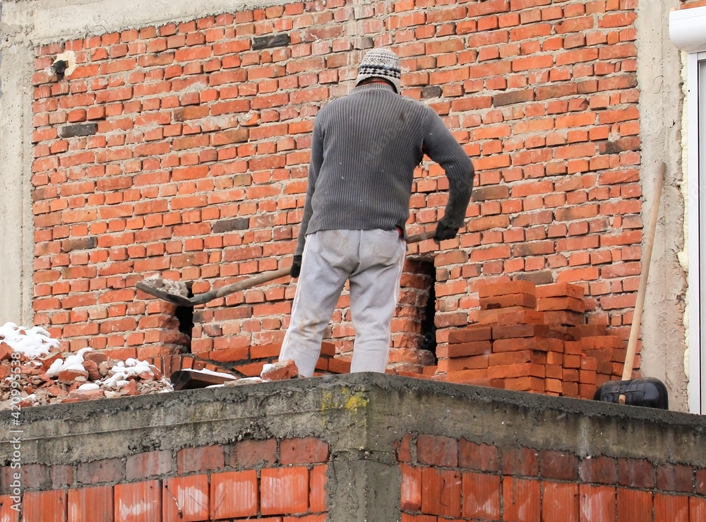 A man shovels removes debris of a drilled hole in the wall