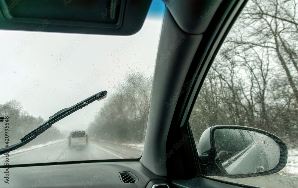 Naklejka premium Car wipers wiping the windshield. Winter highway during snowfall
