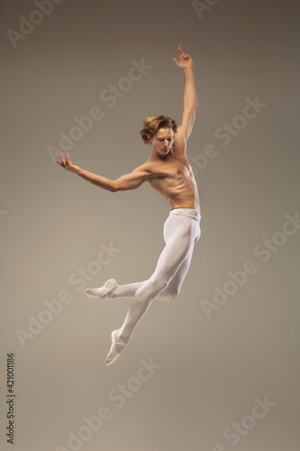 Fototapeta Naklejka Na Ścianę i Meble -  Aesthetic. Young and graceful ballet dancer isolated on studio background in flight, jump. Art, motion, action, flexibility, inspiration concept. Flexible caucasian ballet dancer, moves in glow.
