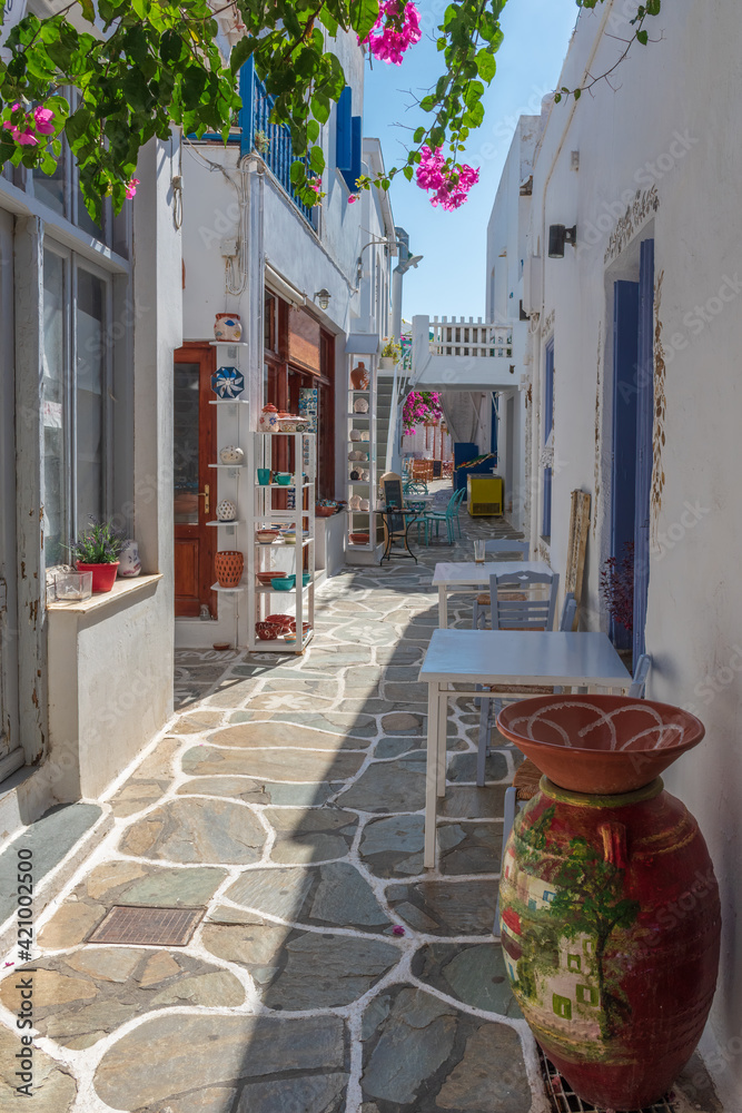 Obraz premium Cycladitic alley with a narrow street and an exterior of a traditional whitewashed cafe with chairs and tables in Chora kythnos,cyclades, Greece.
