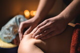 Massage of a female back in a dark room of a spa salon. Male masseur doing massage of the back of the body and lower back