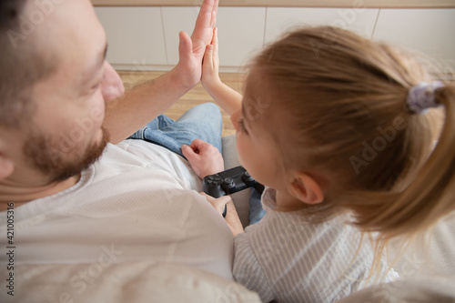 young man father giving high five to happy little child daughter after finishing video game. Joyful two generations family celebrating successful win, playing together in living room. Back view.