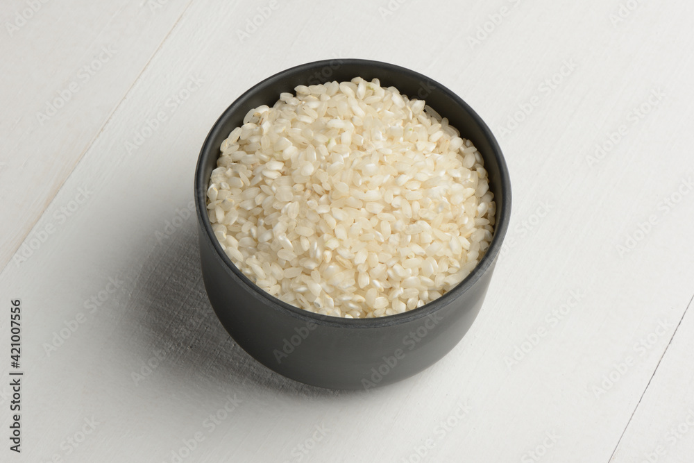 Arroz redondo en un bol de cocina negro en la mesa blanca Arroz redondo en un bol de cocina negro en la mesa blanca