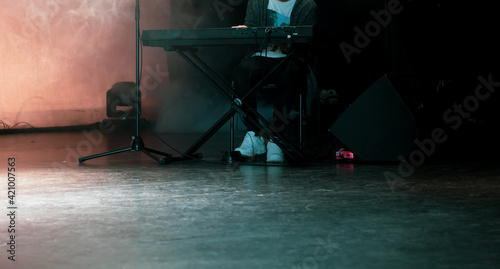 Pianist playing on electric piano in a dark concert hall with smoke. Pianist sitting playing piano in a dramatic concept. Red and turquoise lights, tones. Smoke background. 
