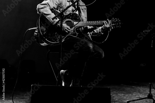 Male musician playing guitar on stage. Black and white high contrast. Pop singer doing a live, instrumental, acoustic concert. Unrecognizable person. Grunge concept. Black background
