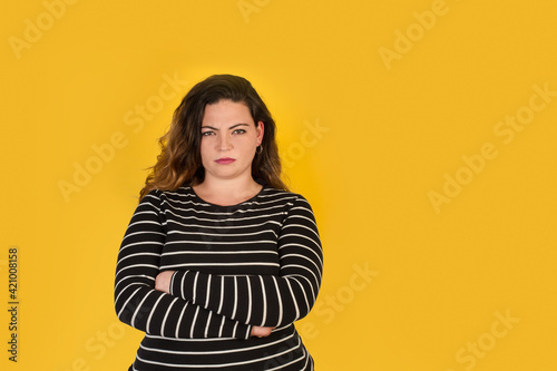 Obraz na płótnie Mujer joven con cara de enfado y brazos cruzados sobre un fondo amarillo liso y aislado