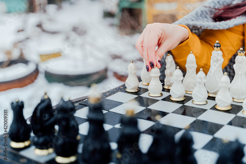 Selective focus of beautiful chess on chessboard. Close up of body part of unrecognizable woman playing in board game on street.