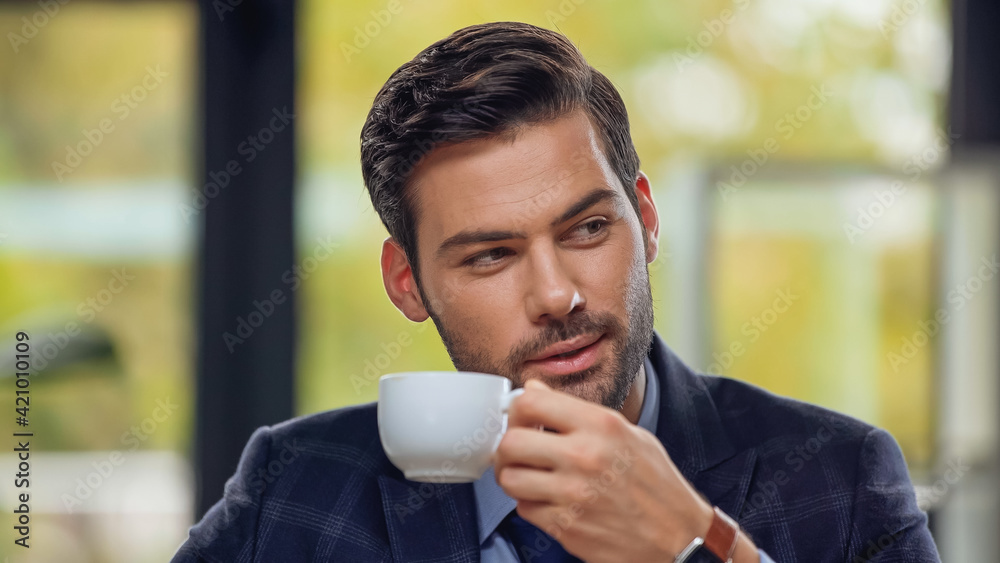 handsome businessman holding cup of coffee and looking away handsome businessman holding cup of coffee and looking away
